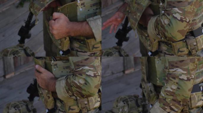 一名穿着迷彩制服的难以辨认的男性士兵的手特写，他正准备进行军事演习或战斗。军人紧固他的防弹衣。乌俄战