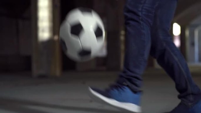 手持动作射击: 专注于有才华的年轻足球运动员巧妙地玩弄球的腿。男子在地下停车场展示他的自由式足球技巧