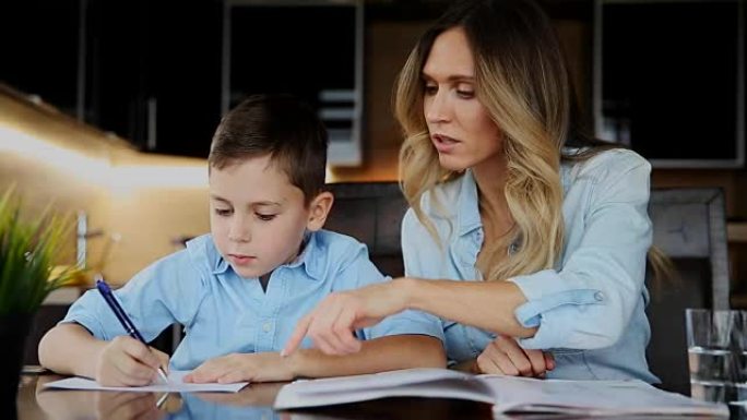 微笑的母亲帮助儿子做作业，口述课文帮助您在厨房的桌子旁写字
