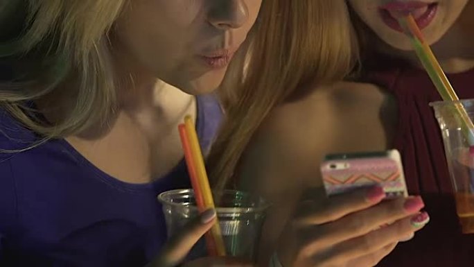 两个醉醺醺的女性朋友一边喝着鸡尾酒一边在智能手机上发信息