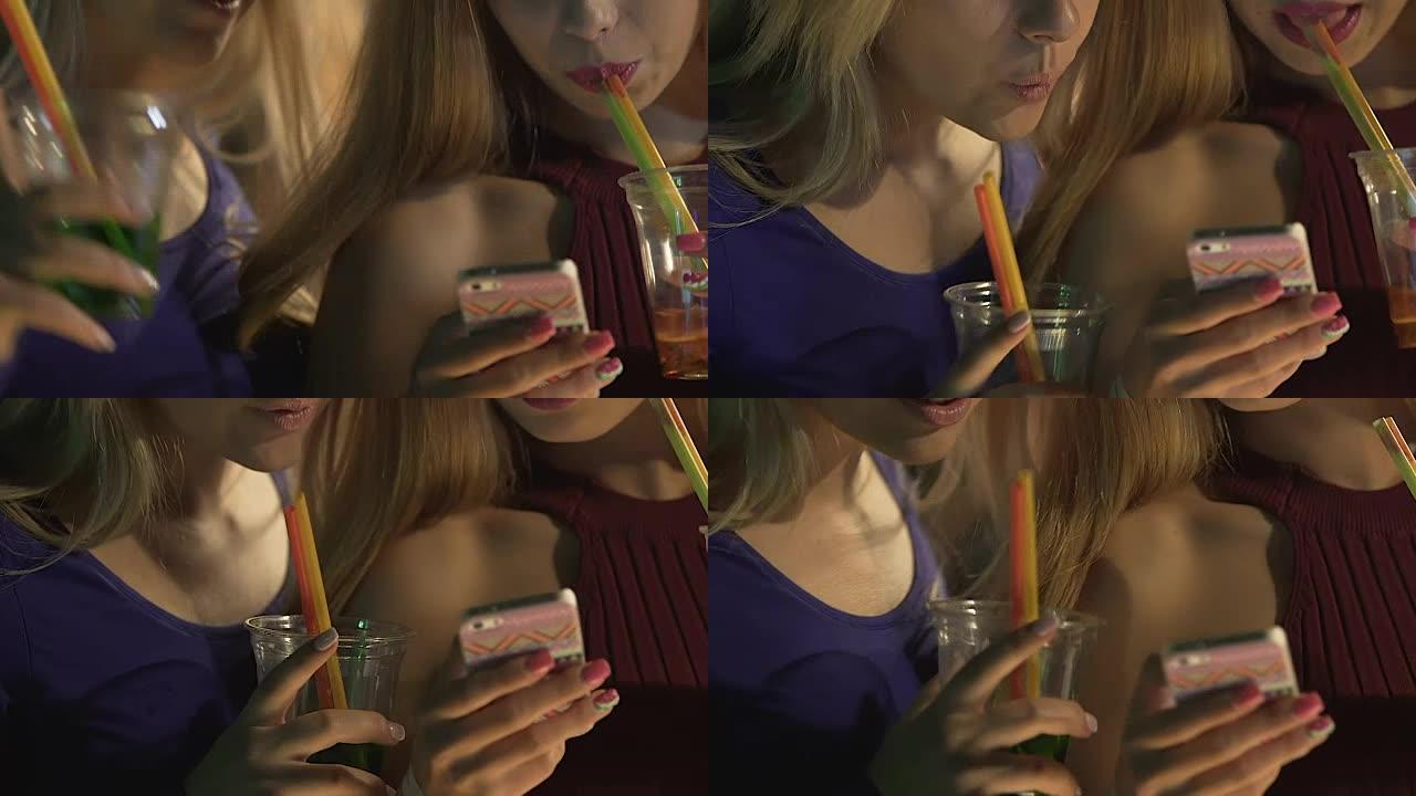 两个醉醺醺的女性朋友一边喝着鸡尾酒一边在智能手机上发信息