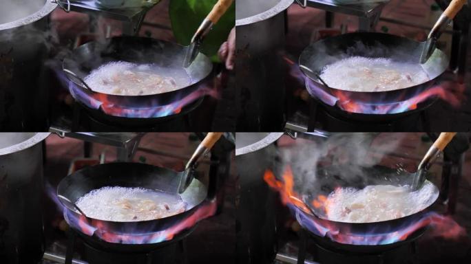 曼谷唐人街的街边炒锅大火。库克晚上在泰国Yaowarat路美食街市中心的马路上向外面的蔬菜燃烧热油。