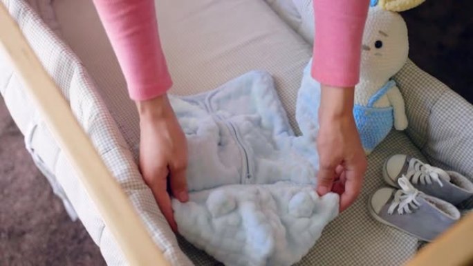 未来的母亲将男婴的新衣服放在木制婴儿床，童鞋，针织兔子玩具和婴儿床内的超声波性别图片，父母身份和家庭