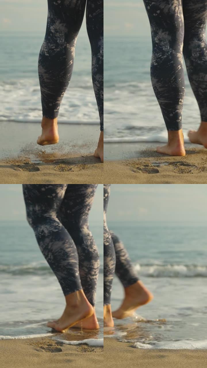 一个穿着紧身裤的年轻女子的腿，在沙滩上，水的泡沫碰着她的腿。垂直视频社交媒体