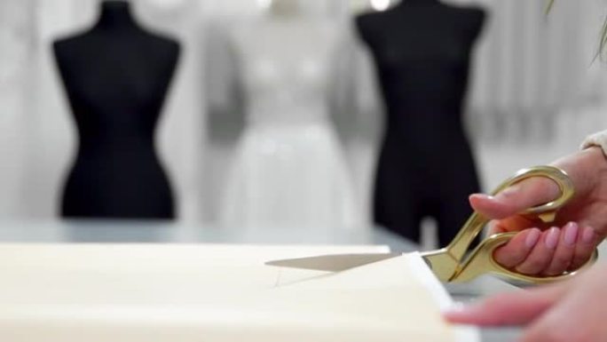 美丽的时装设计师女孩在纸上剪下金色剪刀图案，穿着婚纱的模特背景面料。婚纱制造商