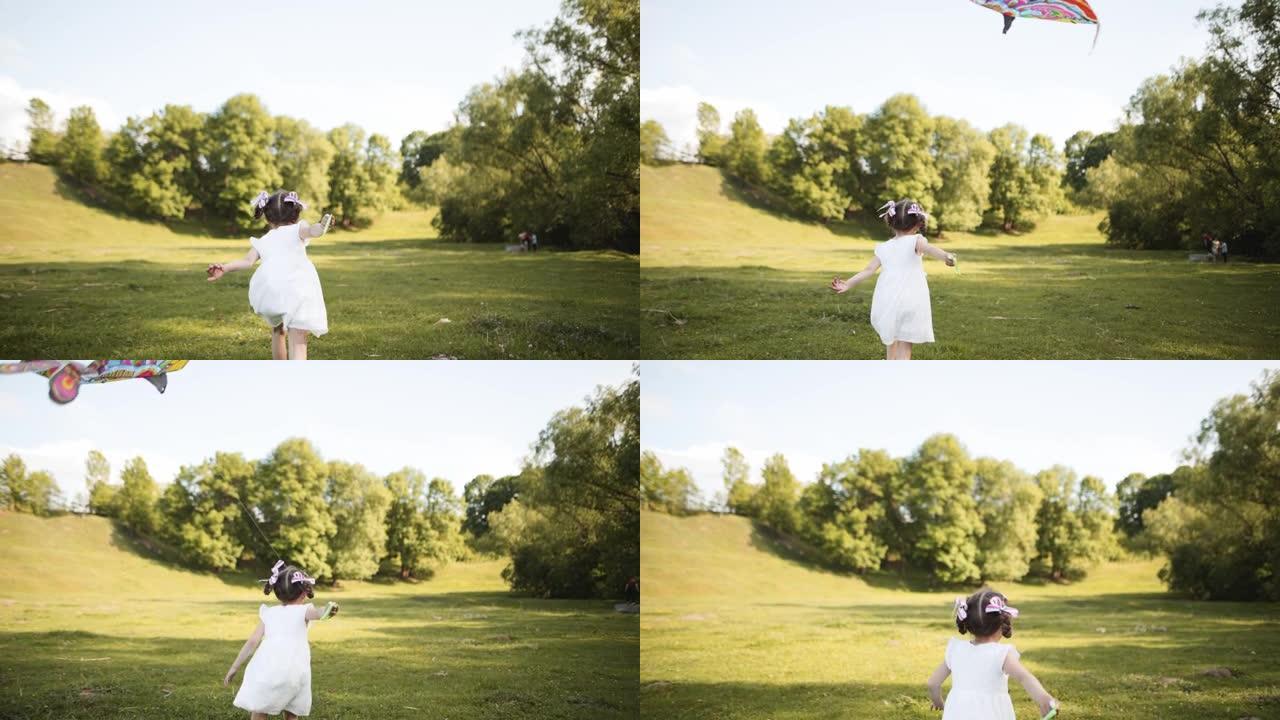 快乐的孩子放风筝。夏天，女孩在公园的绿草地上奔跑。日落时，孩子在田野里玩耍。孩子随风将风筝射向天空。