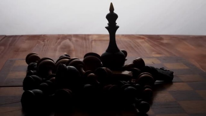 国际象棋棋子黑皇后站在棋盘上，周围是其他躺着的棋子。棋盘游戏。有点运动。摄像机沿着物体移动