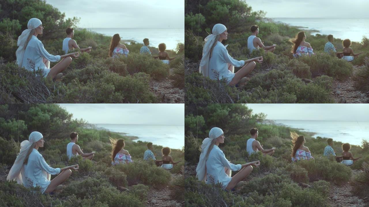 各种各样的人坐在蓝色大海旁的草崖上放松身心。莲花姿势冥想并练习健康