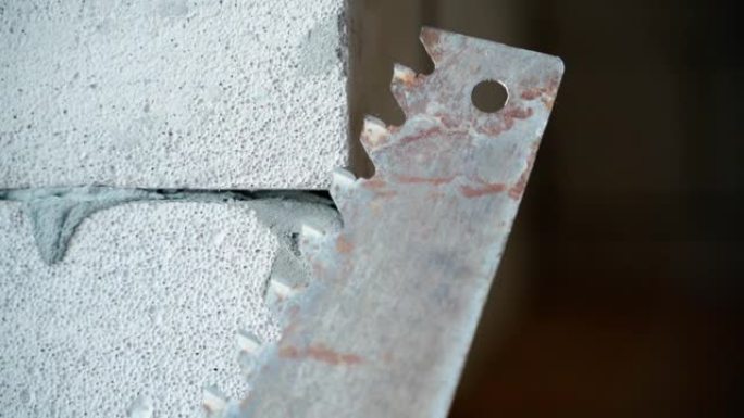 一种旧的手动钢锯，用于在加气混凝土砖墙的背景下进行加气混凝土特写。锯和气体块