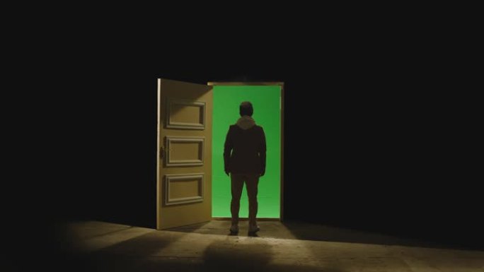 一个男人走在敞开的门前，后面黑暗。商人在靠近门的地板上走绿屏的镜头。匿名、商业梦想或传送的概念