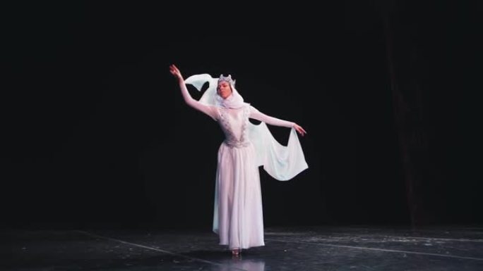 一位优雅，勤奋的芭蕾舞演员戴着皇冠，在黑色背景上摆出美丽的姿势。风吹着她漂亮的白色西装。
