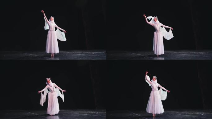 一位优雅，勤奋的芭蕾舞演员戴着皇冠，在黑色背景上摆出美丽的姿势。风吹着她漂亮的白色西装。