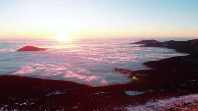 白雪皑皑山脊的空中无人机视图，日落之后的云层上方