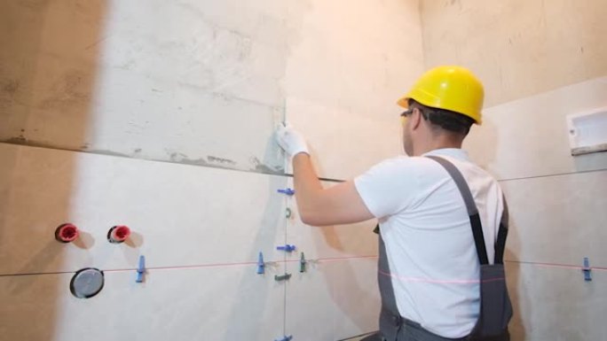 男工人是浴室铺设瓷砖的师傅。修理工安装现代大瓷砖。