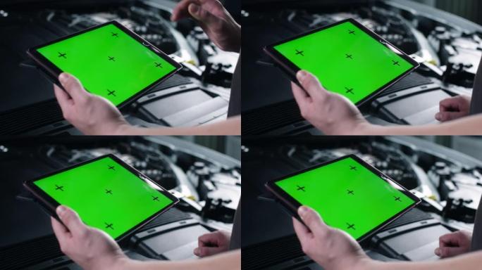 一位不知名的男性汽车服务人员站在打开的引擎盖附近，用绿色屏幕的数码平板电脑检查汽车并进行维护