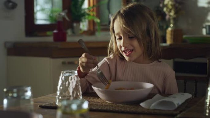 一个可爱的小女孩的肖像，午餐吃美味的意大利面，并感谢她的母亲做饭。快乐的女孩子坐在厨房里享受家常饭
