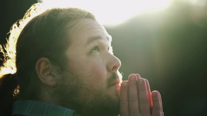 精神青年在户外向上帝祈祷。侧面脸接近一个胖乎乎的休闲男性在祈祷感觉存在一个更高的力量。希望与信念的概