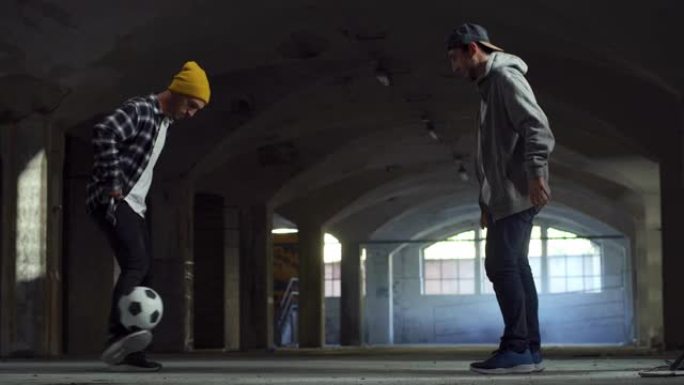 两名职业足球运动员用球表演自由式足球技巧的动作镜头。自信的年轻足球运动员和男性朋友在地下停车场炫耀杂
