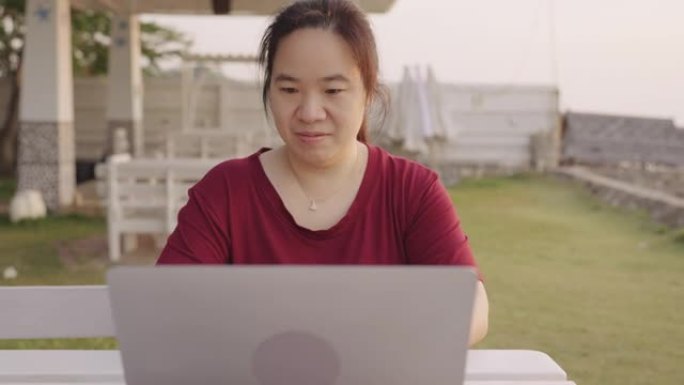亚洲妇女在海滩旅行时在笔记本电脑上工作