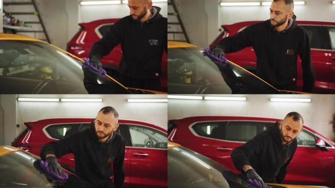 选择性关注洗车工人的手，戴防护手套，用超细纤维布清洁现代黄色车窗。汽车细节或车辆概念。清洁现代车窗。