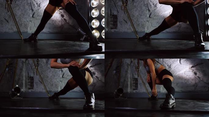 穿着性感衣服的运动女孩在石墙的背景上进行健身，依次蹲下每条腿训练大腿。残酷的环境