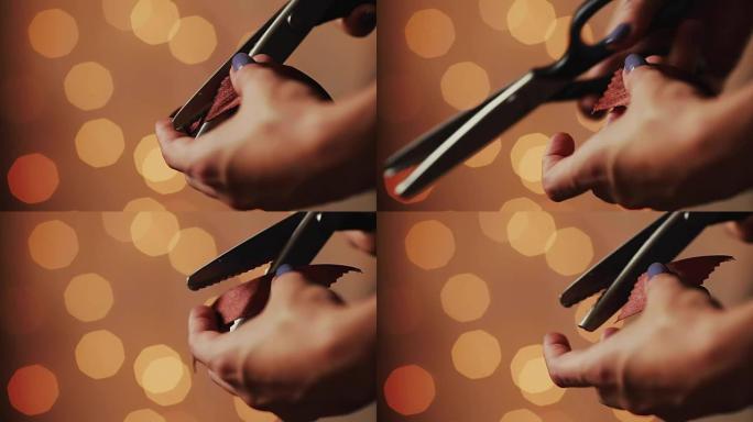 女性双手的特写，剪彩，为您所爱的人制作圣诞手工礼物。在模糊的灯光花环的背景上。博克
