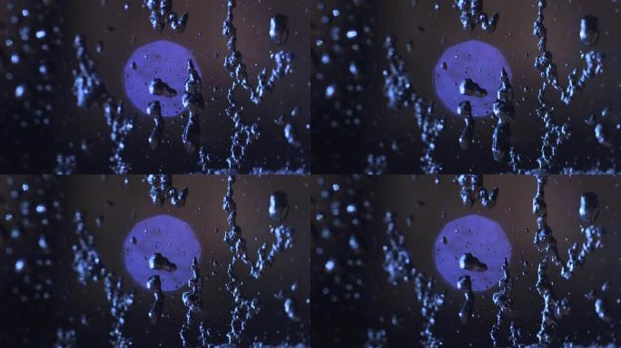 重滴融化连接的特写镜头，在黑暗的背景上流下。圆形蓝色高光。月光模糊。