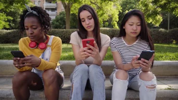 三个年轻严肃的女人在户外用手机。同事们在手机上看期末成绩。