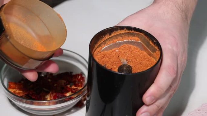 一个人在咖啡研磨机里磨干红辣椒。演示在咖啡研磨机中的研磨程度。研磨辣椒。特写。