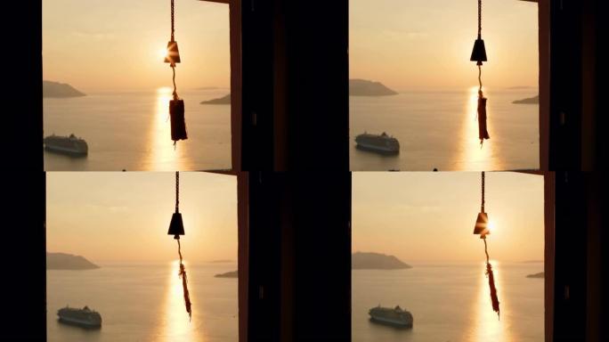 风铃挂在窗户上，在背景中，海洋或海洋上有美丽的日落，阳光照进相机。门口挂着带音符的铃铛。