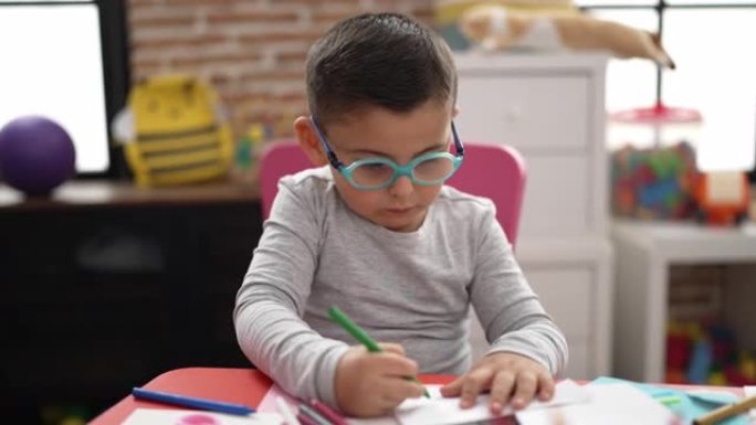 可爱的西班牙裔蹒跚学步的学生在幼儿园的笔记本上画画