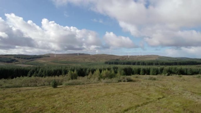空中无人机画面缓慢上升，揭示了苏格兰风电场中的多个转弯风力涡轮机，该风电场被苏格兰阿盖尔金泰尔半岛的
