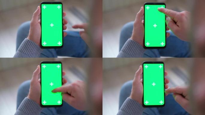 年轻人坐在家里，手里拿着智能手机绿色模拟屏幕。男性使用色键手机。垂直模式。触摸，滑动显示，点击，浏览