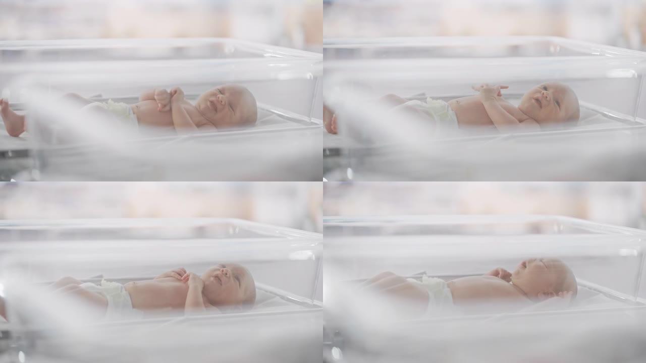 可爱的高加索新生婴儿躺在产科医院孵化器的摇篮里。一个顽皮而充满活力的孩子的肖像。医疗保健、怀孕和孕产
