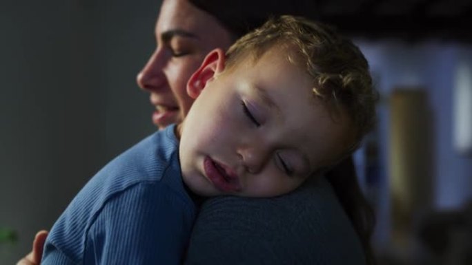 一个年轻女子在家里给昏昏欲睡的儿子唱摇篮曲的肖像。深情的母亲让她的男小孩入睡，揉着他的背，用温柔的歌