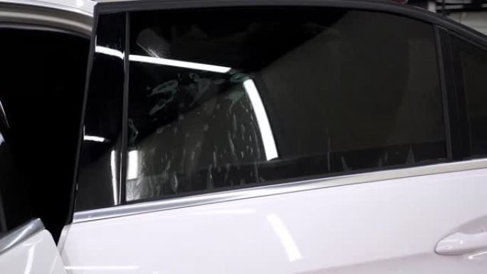 一位特写机械师在汽车玻璃上安装了一层着色膜，他用刮刀。