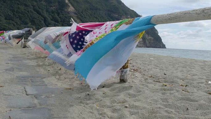 彩色沙滩巾挂在木制栏杆上，在傍晚的海滩上随风摇曳