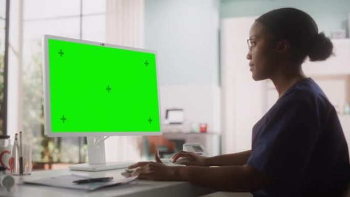 一位美丽的黑人女性医疗保健专业人员在医院绿屏色度键显示的电脑上工作的肖像。诊所护士长正在更新电子健康