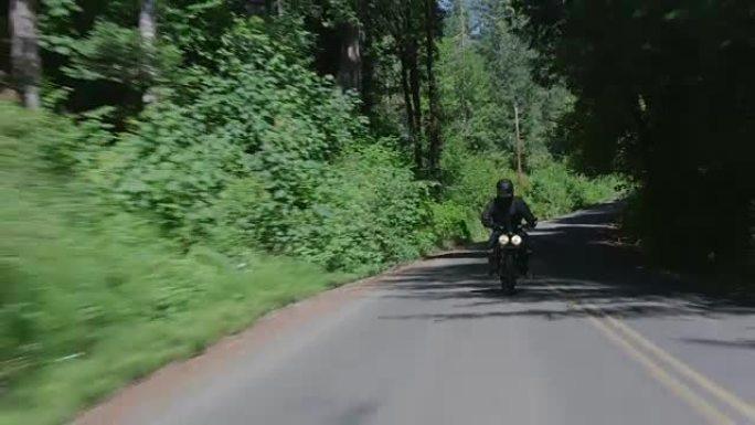 在乡村公路上骑摩托车的男子的跟踪镜头。