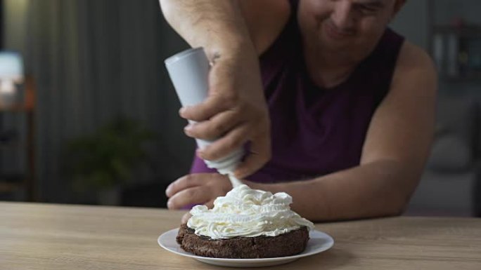 肥胖的男人用鲜奶油装饰巧克力蛋糕，不健康的食物