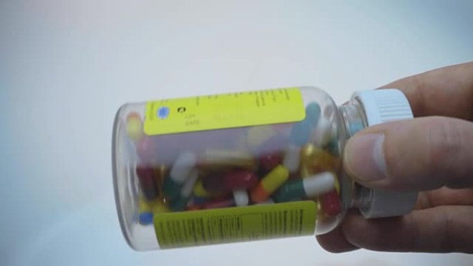 在一个透明的塑料瓶中，一个人用药物摇动彩色胶囊