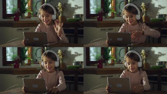 一个可爱的小女孩在厨房里用数字平板电脑和耳机与家人进行视频通话的肖像。使用技术与朋友保持远程联系的女