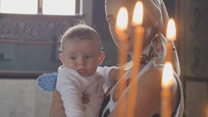 教堂里蜡烛前有小儿子的年轻母亲肖像