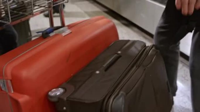 男子从机场的行李传送带上拿一个旅行包，放在行李车上