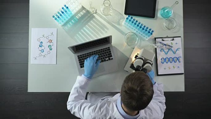 科学家在显微镜下观察样品并在实验室的笔记本电脑上书写结果