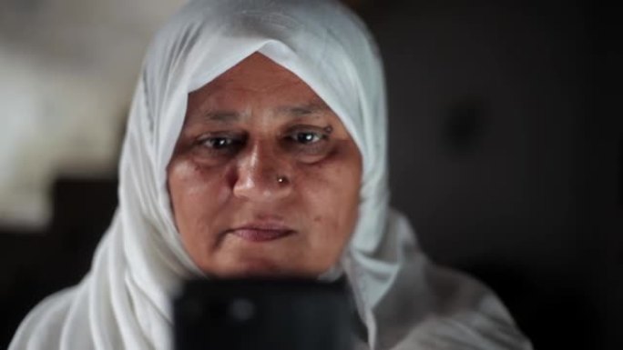 穿着白色头巾的穆斯林妇女使用黑色手机微笑。穆斯林妇女使用技术。