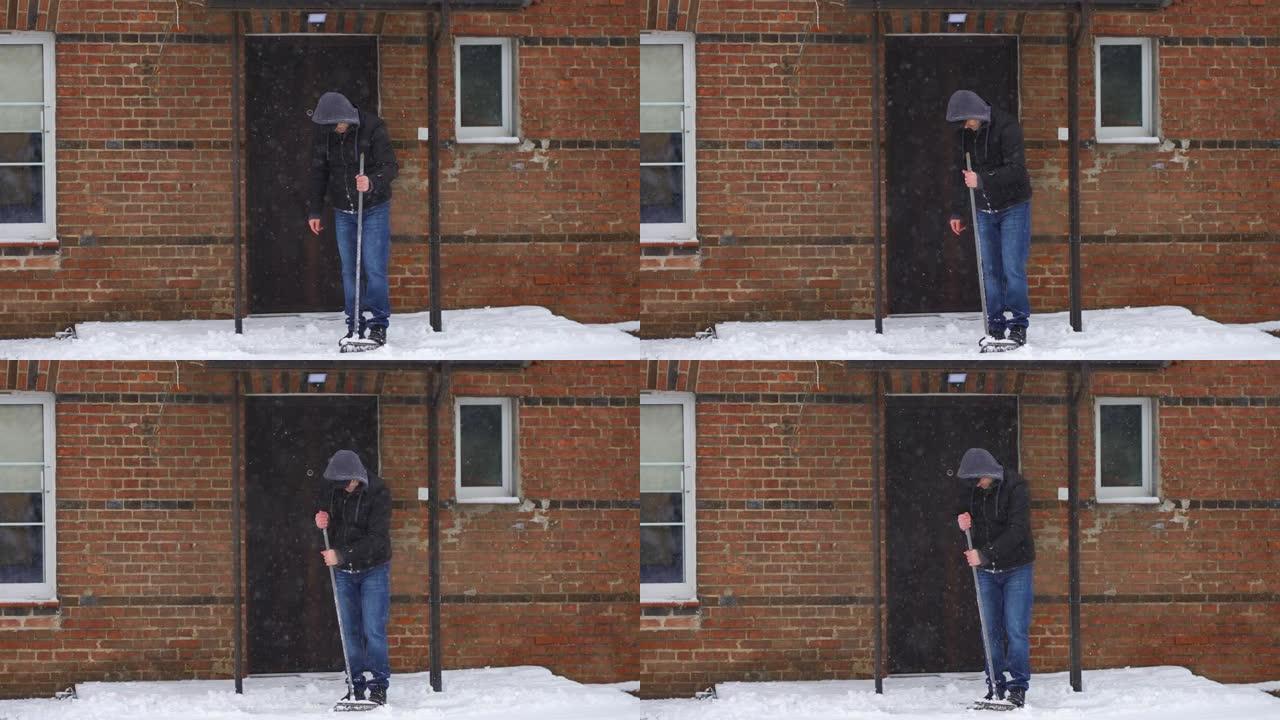在大雪旋风慢动作中，穿着连帽衫的男子在清理房屋院子后看着破刷子