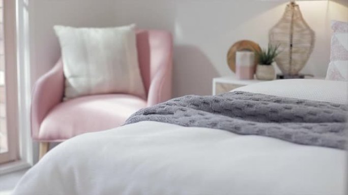 漂亮的卧室里有一把舒适的粉色椅子，早晨的阳光透过窗户流到柔软舒适的床上，床上铺着绗缝毯子。