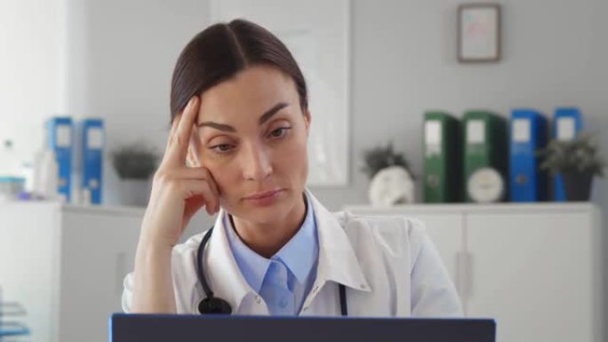 精疲力尽的年轻女医生坐在笔记本电脑前的办公室里，眼睛疲劳