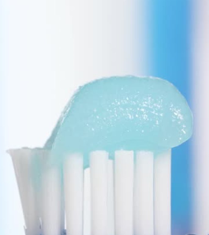 牙刷和牙膏。蓝色牙刷的垂直宏观视图，上面有水滴，牙膏被挤压在蓝白色背景上，有复制空间。慢动作